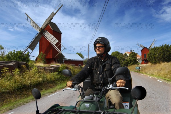 Man riding on ATV along a road with distinctive windmills, Långnäs, Åland, Finland
