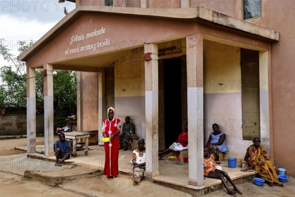 People sit and stand in front of a hospital building. The surrounding area seems quiet, Bouké, region, Côte d'Ivoire