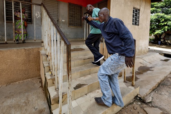 Nurse Albert helps a patient climb stairs, Bouaké, Nimbo, Côte d'Ivoire