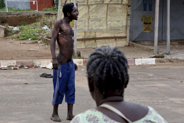 Mentally ill homeless person stands in the street while a woman sits nearby, Bouaké, Côte d'Ivoire