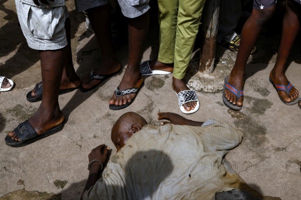 A homeless man lies asleep in the street surrounded by people, CI Bouaké, Ivory Coast