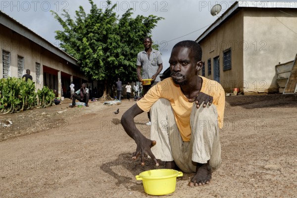 A patient sits with a bucket in the courtyard of a male psychiatric ward, Bouaké, Nimbo, Côte d'Ivoire