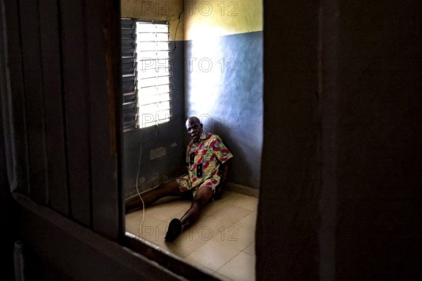 A man sits alone in a room at Saint Camille men's psychiatry, Bouaké, Côte d'Ivoire