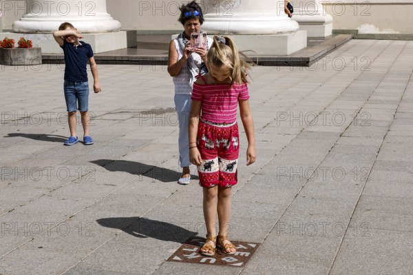 Child standing on miracle tile while tourists capture the moment, Vilnius, Vilnius County, Lithuania