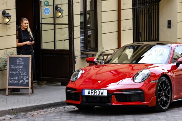 Woman standing next to a red car in front of a cafe in Uzupis, Vilnius, Vilnius County, Lithuania