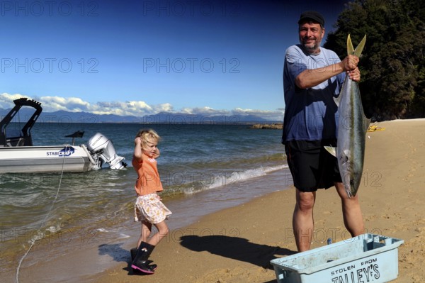 A man keeps a big fish on the beach in Appletree Bay, Abel Tasman National Park, South Island, New Zealand