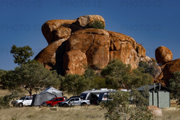 Campground surrounded by distinctive red rocks and vehicles under blue skies, Devil's Marbles, Northern Territory, Australia