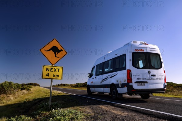 A motorhome drives along the Great Ocean Road past a kangaroo warning sign under clear blue skies, Great Ocean Road, Victoria, Australia