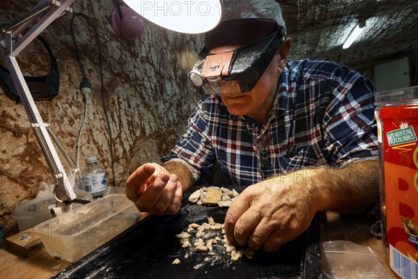 Miner examining opals at work light at Tom's Working Opal Mine, Coober Pedy, South Australia, Australia