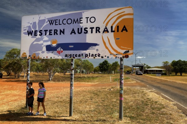 Two people pose in front of a welcome sign on the border with Western Australia, zero