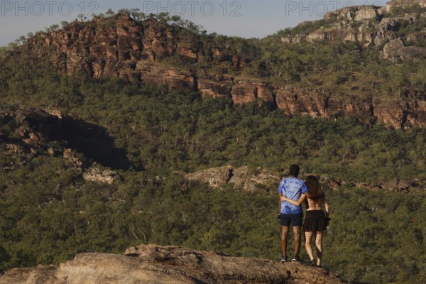 Two people on a rock with a view of wooded rocky landscape, Nawurlandia, Northern Territory, Australia