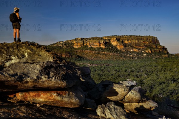 Tourist stands on a rocky plateau overlooking impressive rock walls in the evening sun, Nawurlandia, Kakadu National Park, Australian Northern Territory