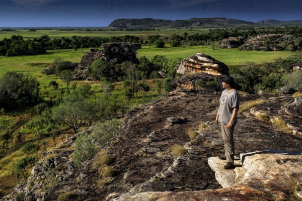 Person standing on a rocky outcrop with a wide view of green countryside, Ubirr, Northern Territory, Australia