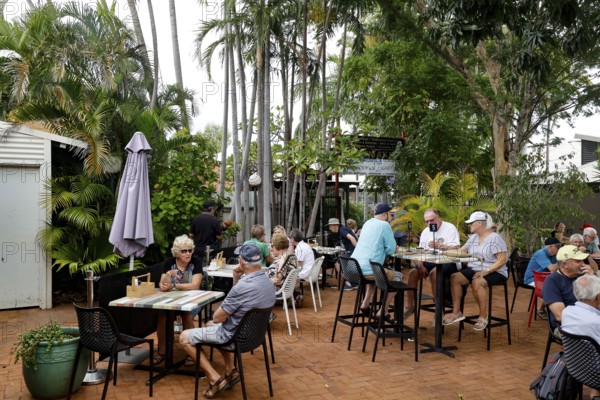People eat and relax in Chinatown open-air café surrounded by palm trees, Broome, Western Australia, Australia