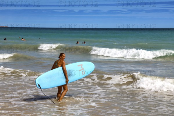 Surfer with blue surfboard standing on the water of Cable Beach, Broome, Western Australia, Australia