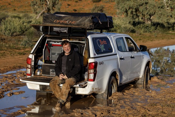 Man sits relaxed in the open trunk of a muddy off-road car on the Old Andado Track