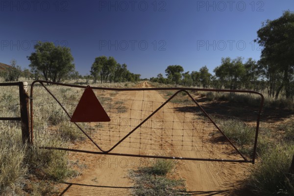 Metal gate on sandy desert road with trees in background