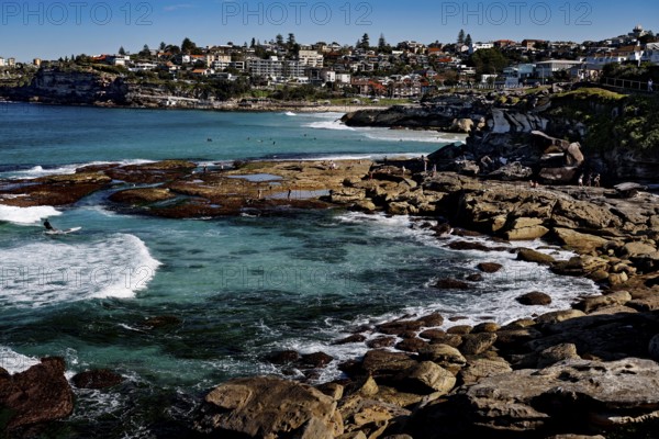Tamarama Point with rocky shores and clear waves off coast occupied by houses, Sydney, New South Wales, Australia