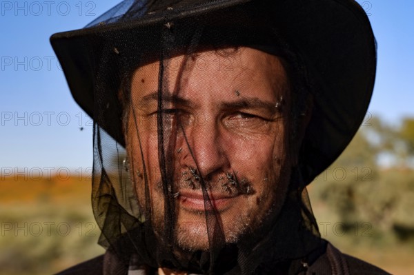 Man with a fly net over his face in front of a clear sky