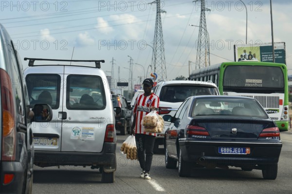 Hustle and bustle in Abidjan with cars stuck in traffic and a person crossing the road, Abidjan, null, Côte d'Ivoire