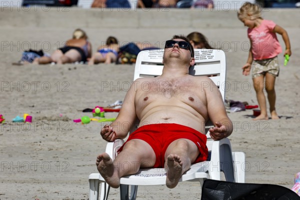 A man wearing red swimming trunks is relaxing on a lounger on a sandy beach, Pärnu, Estonia