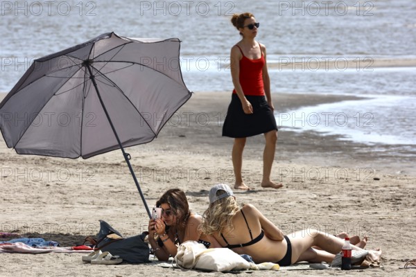 Two woman relaxing under a large sunshade on a sunny beach, Pärnu, Estonia