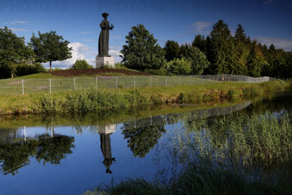 Socialist statue in Grutas Park is reflected in a calm body of water surrounded by trees, Druskininkai, Lithuania