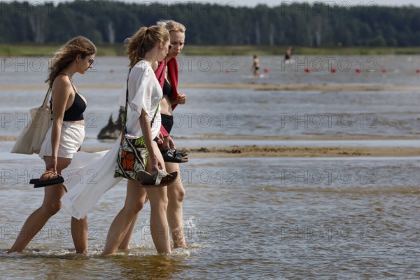Three woman walking in the shallow water of a beach surrounded by vast nature, Pärnu, zero, Estonia