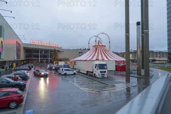 Shopping center parking lot in case of rain with illuminated circus tent at dusk, Böblingen, Germany