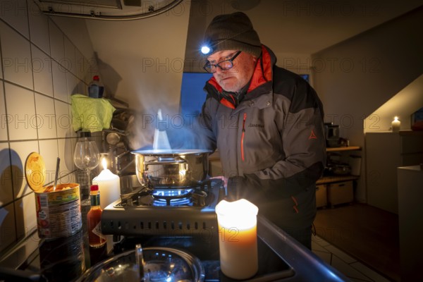 Symbolic picture blackout, extensive, prolonged power failure, in private settings, without electricity, heating, water, cooking in the kitchen, heating food with a gas-powered camping stove, which is also approved for indoor use
