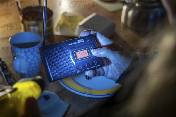 Symbolic blackout, extensive, prolonged power failure, in private surroundings, without electricity, heating, water, family at the dining table with warm winter clothes, sleeping bag, battery-operated radio, only source of information, no TV, Internet, mobile phone, light from battery lights, flashlights, food from cans, ready meals, heated on the camping stove, limited supply of food