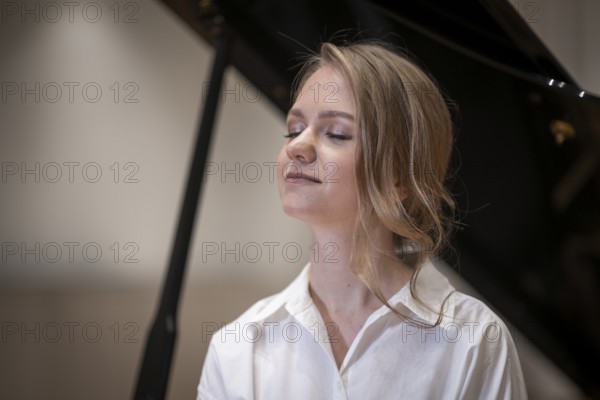 Dreamy looking young woman, pianist, wearing white blouse in front of Steinway & Sons grand piano, Stuttgart, Baden-Württemberg, Germany