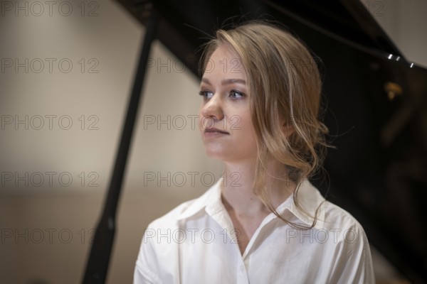 Serious looking young woman, pianist, wearing white blouse in front of Steinway & Sons grand piano, Stuttgart, Baden-Württemberg, Germany