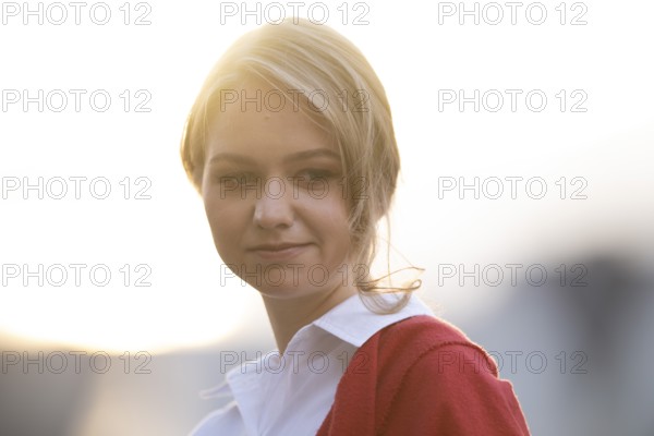 Serious looking young woman in white blouse and red cardigan, in backlight, Stuttgart, Baden-Württemberg, Germany