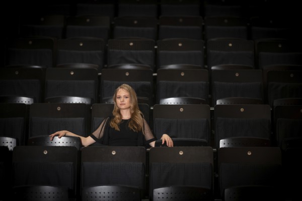 Young woman, pianist, in evening dress, sitting on chair in audience area, Stuttgart, Baden-Württemberg, Germany