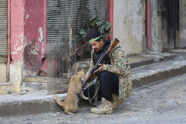 In Aleppo, Syria on January 10, 2026, a Syrian Army soldier crouches to pet a stray cat in the street following intense battles with SDF forces in the Sheikh Maqsoud and Ashrafieh neighborhoods after the withdrawal of Kurdish groups towards eastern Syria, Aleppo, Sheikh Maqsood, Syria