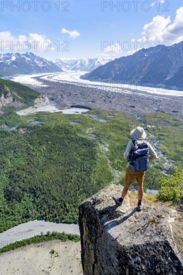 Young man on a rocky outcrop enjoying the view, view of impressive mountain scenery with Matanuska glacier and glaciated mountain peaks, Lion's Head, Chugach Mountains, Alaska, USA