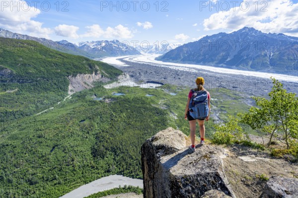 Young woman on a rocky outcrop enjoying the view, view of impressive mountain landscape with Matanuska glacier and glaciated mountain peaks, Lion's Head, Chugach Mountains, Alaska, USA