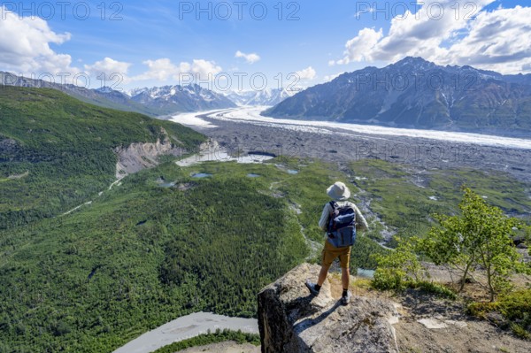 Young man on a rocky outcrop enjoying the view, view of impressive mountain scenery with Matanuska glacier and glaciated mountain peaks, Lion's Head, Chugach Mountains, Alaska, USA