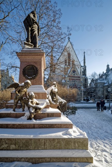 Snowy angel, figure at the Felix Mendessohn Bartholdy monument in winter with snow, Leipzig St. Thomas Church in the back, Leipzig, Saxony, Germany