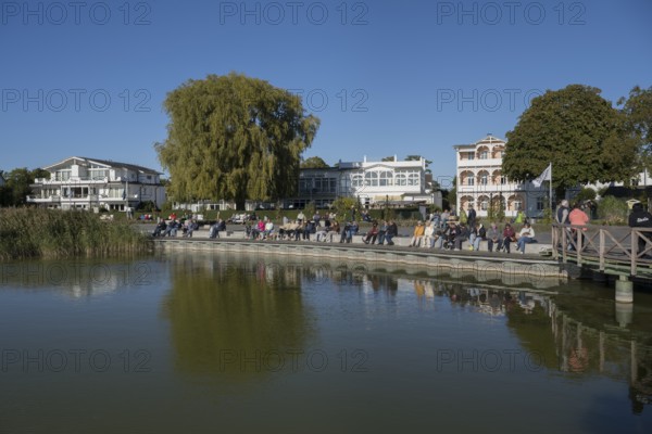 Tourists sunbathe on the promenade of Schmachter See, in the back buildings of spa architecture, Binz, seaside resort, Rügen island, Mecklenburg-Western Pomerania, Germany