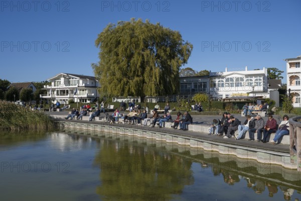 Tourists sunbathe on the promenade, Schmachter See, spa architecture buildings in the back, Binz, seaside resort, Rügen island, Mecklenburg-Western Pomerania, Germany