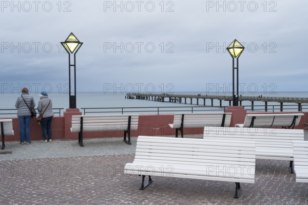 Kurplatz am spa hotel, two people from behind, pier and Baltic Sea behind, twilight, Binz, seaside resort, Rügen island, Mecklenburg-Western Pomerania, Germany