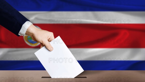 Costa Rica presidential vote 2026. Hand placing a ballot in ballot box with the Costa Rican flag in the background