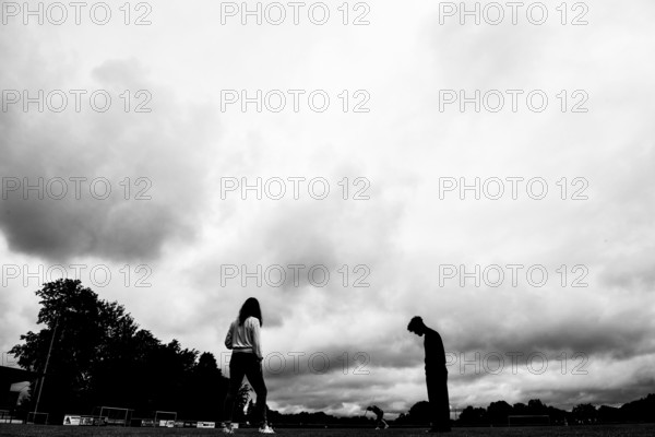 Two silhouettes of people under dramatically cloudy sky on a sports field, sports and fun Olympics Sportfest Schule, Lower Saxony, Germany