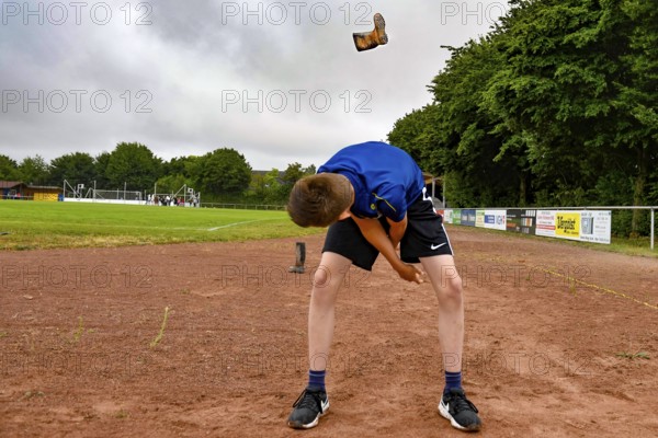 A boy on a sports field throws a rubber boot into the air with effort, sports and fun Olympics Sportfest Schule, Lower Saxony, Germany