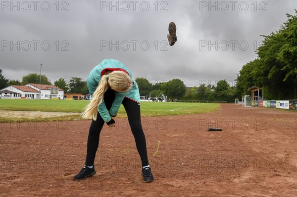 A woman on a sports field throws a rubber boot into the air under a cloudy sky, wellies long throw sports and fun Olympics sports festival school, Lower Saxony, Germany