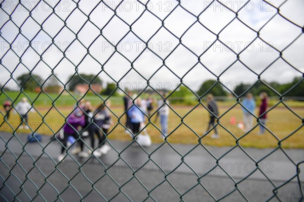 Photographed through a wire fence, a blurred group of spectators is seen on a sports field, Lower Saxony, Germany