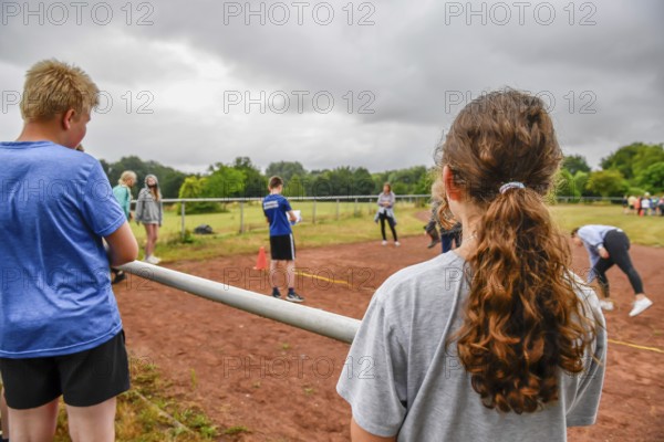 Young people watch a competition on a sports field under cloudy sky, Sport Sportfest Schule, Lower Saxony, Germany