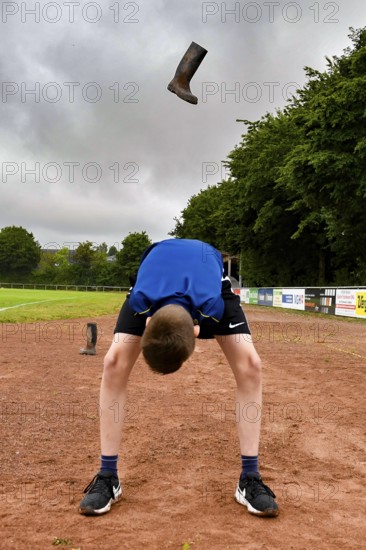 A boy throws a rubber boot high in the air on a sports field rubber boot long throw, sports and fun Olympics sports festival school, Lower Saxony, Germany